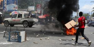 A man holds placards near a burning barricade during a protest against gang-related violence and to demand the resignation of Haiti's transitional presidential council, in Port-au-Prince, Haiti, May 15, 2025. Photo credit: Jean Feguens Regala